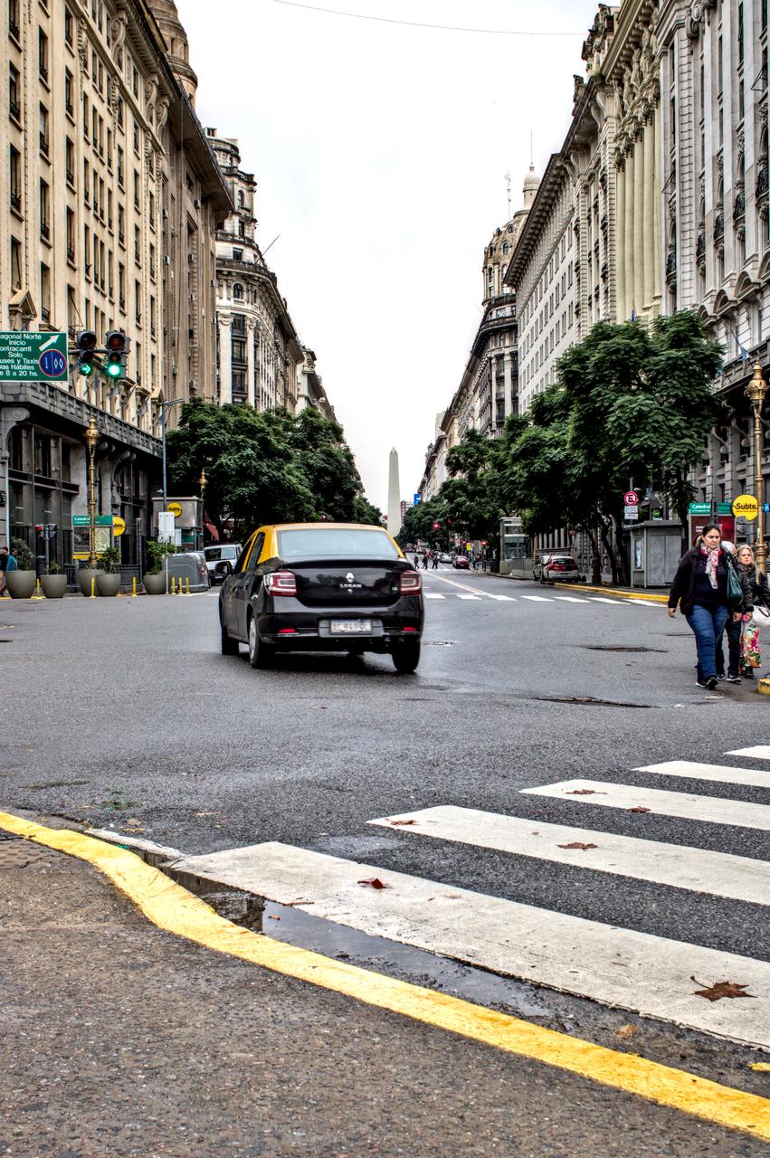 Táxi em rua repleta de edifícios e obelisco ao fundo.