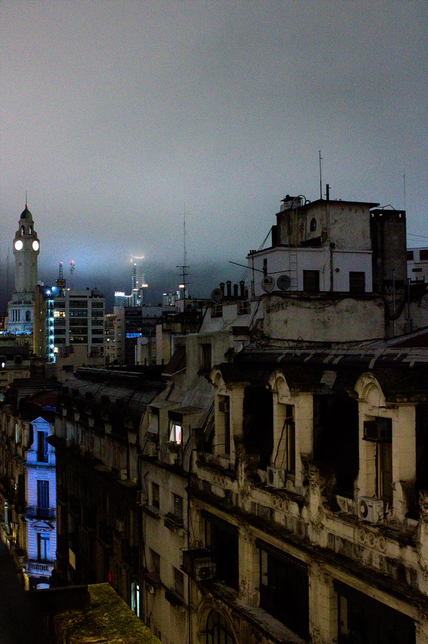 Edifícios envelhecidos e torre de relógio ao fundo, entre a neblina.