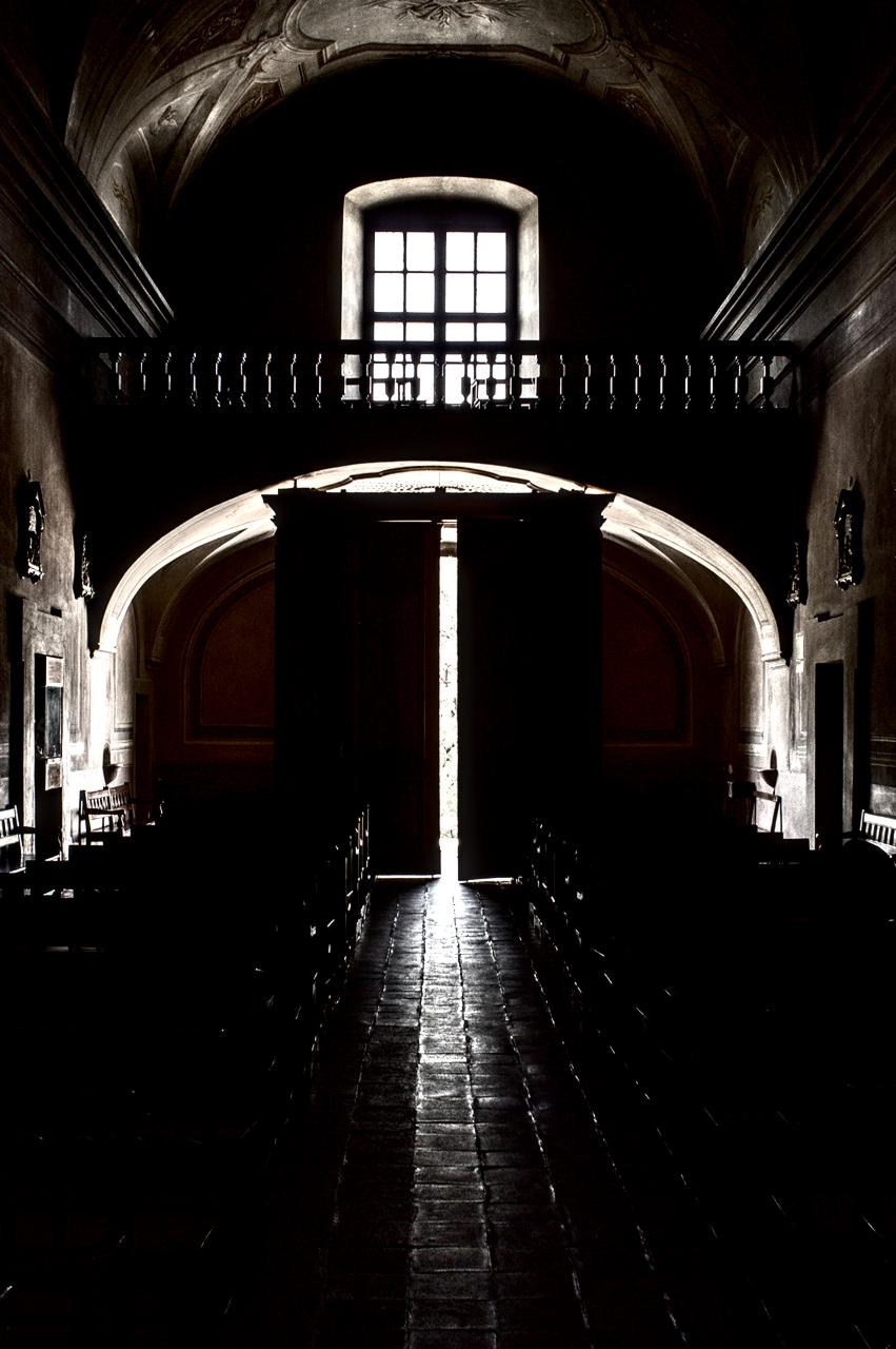 Interior de igreja antiga com porta entre-aberta em contra-luz.