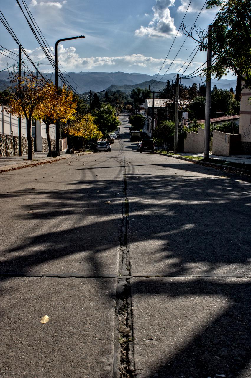 Rua suburbana em ladeira e serras da província ao fundo.