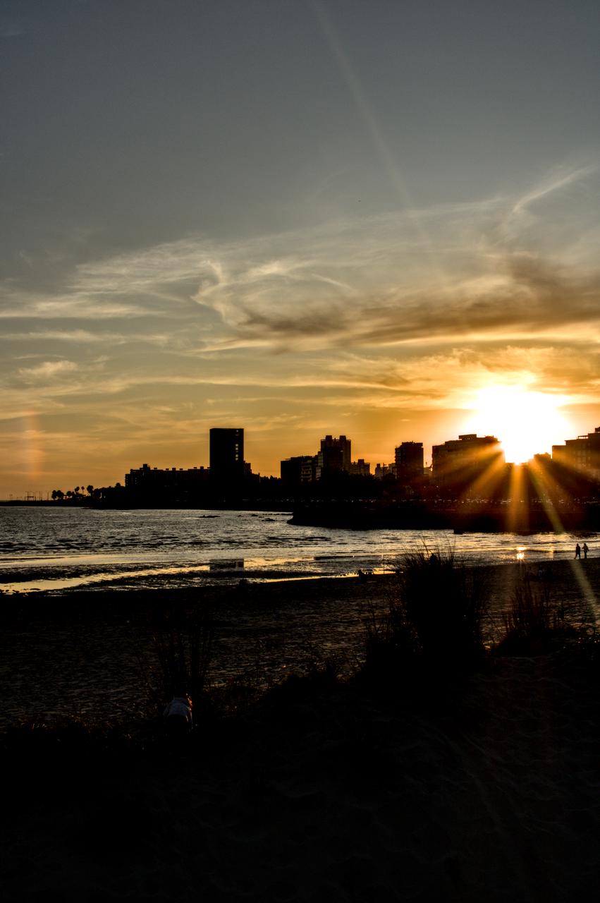 Sol se põe entre prédios diante da praia.