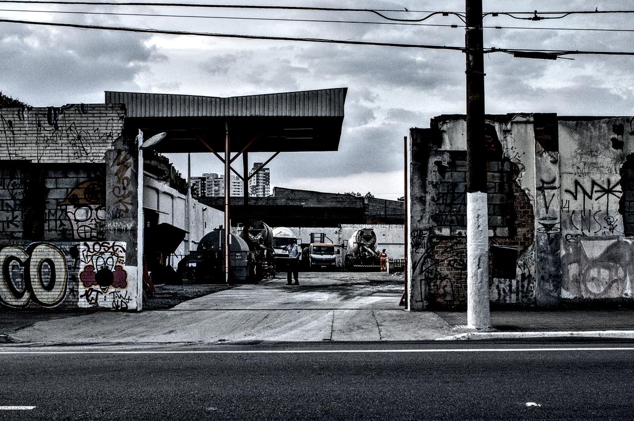 Portão aberto entre paredes antigas com caminhões e homens trabalhando.