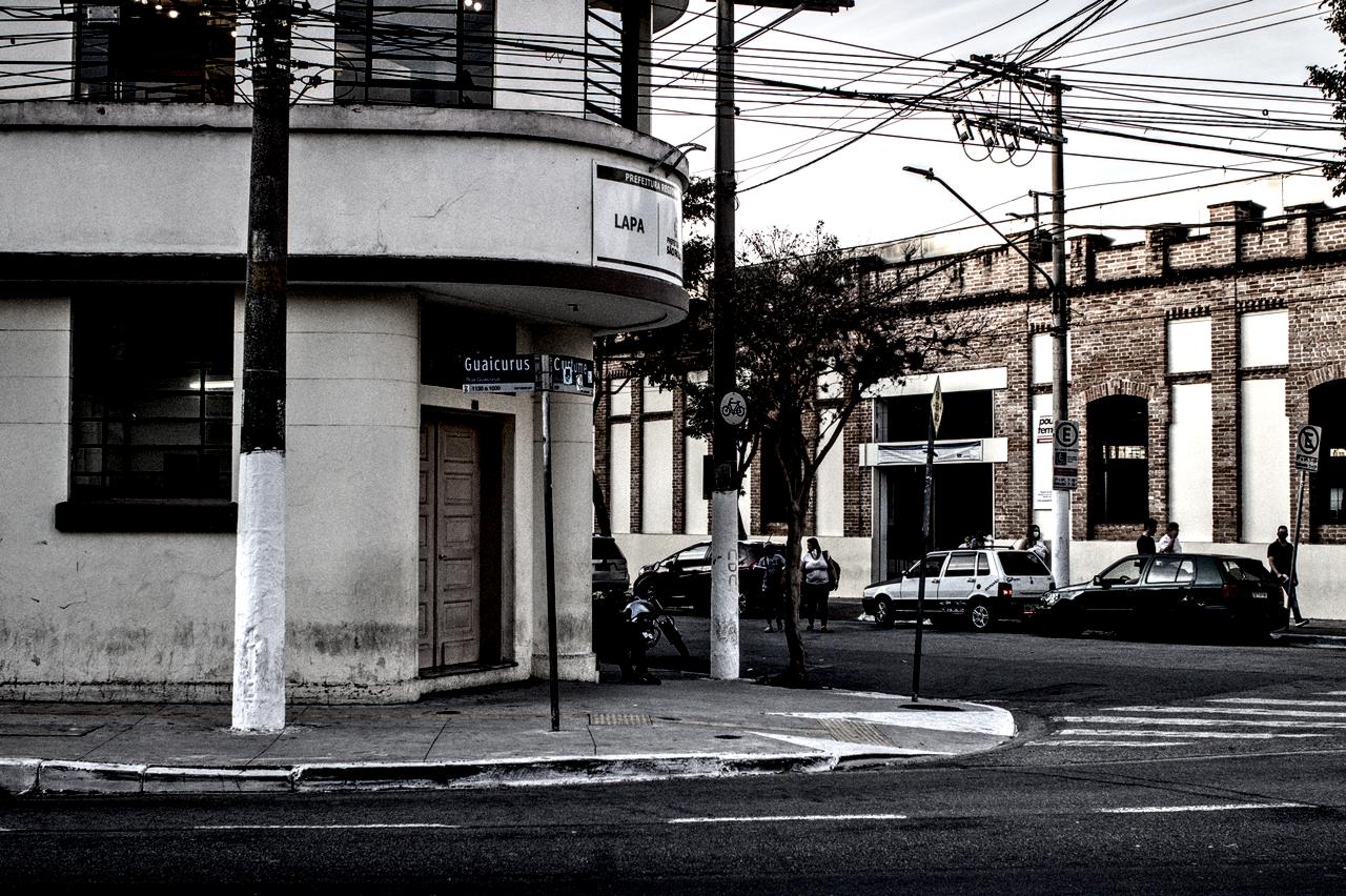 Entrada de edifícil art-déco em pirmeiro plano e, ao fundo, construção de tijolos