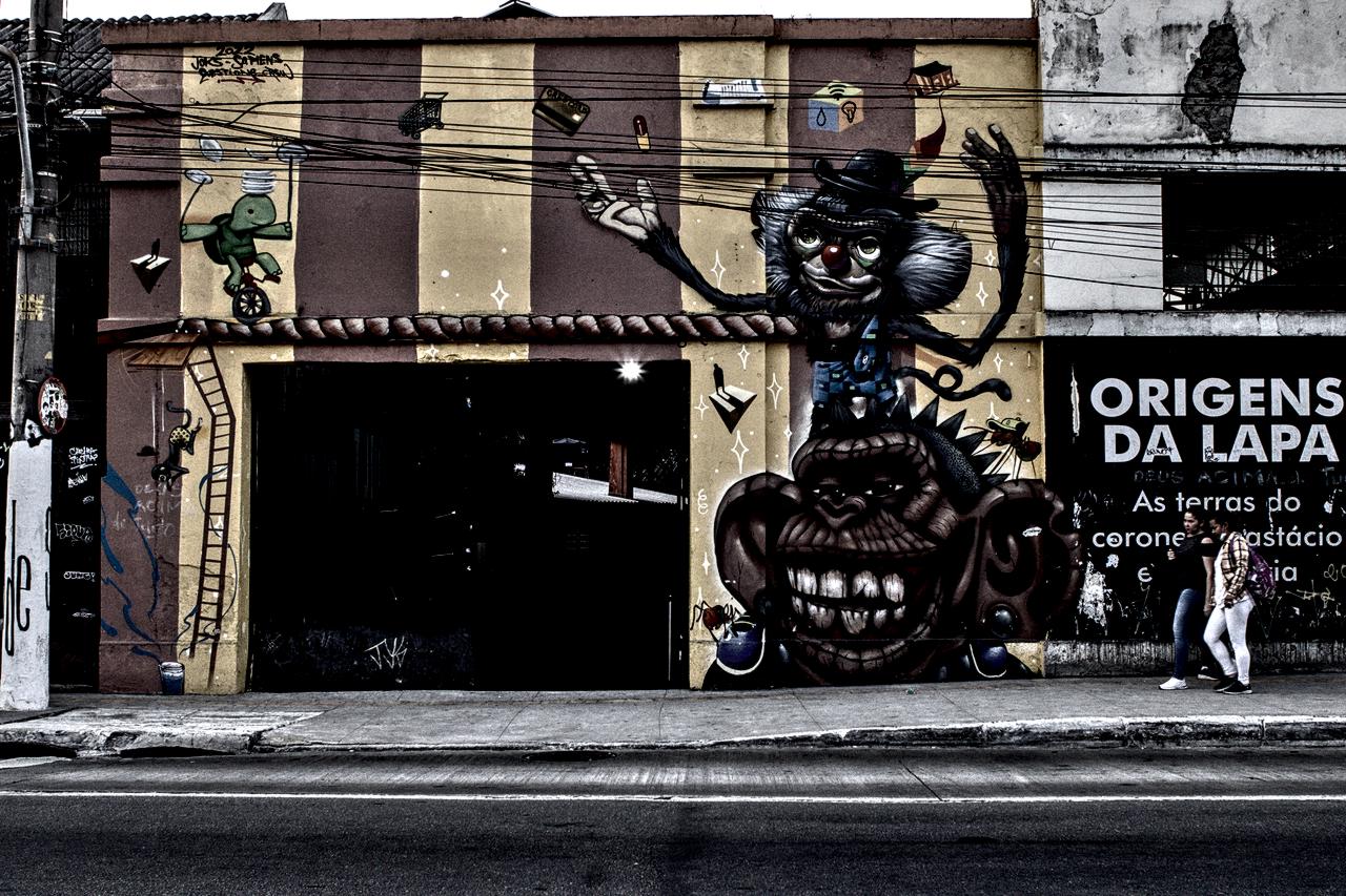 Parede listrada com entrada escura e painel 'ORIGENS DA LAPA'.