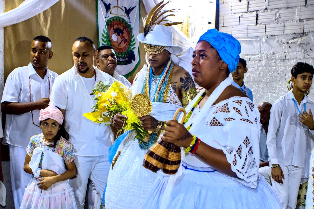 Mulher vestida em branco e rosa ao lado de jovem Logunedé.