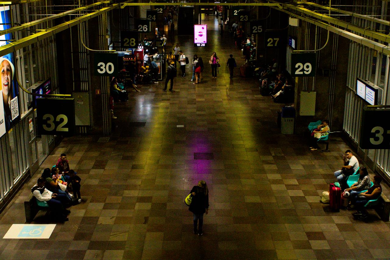 Espaço amplo com idosa caminhando ao centro, sobre reflexo roxo.