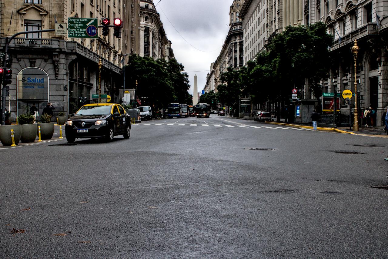 Táxi em rua repleta de edifícios e obelisco ao fundo.