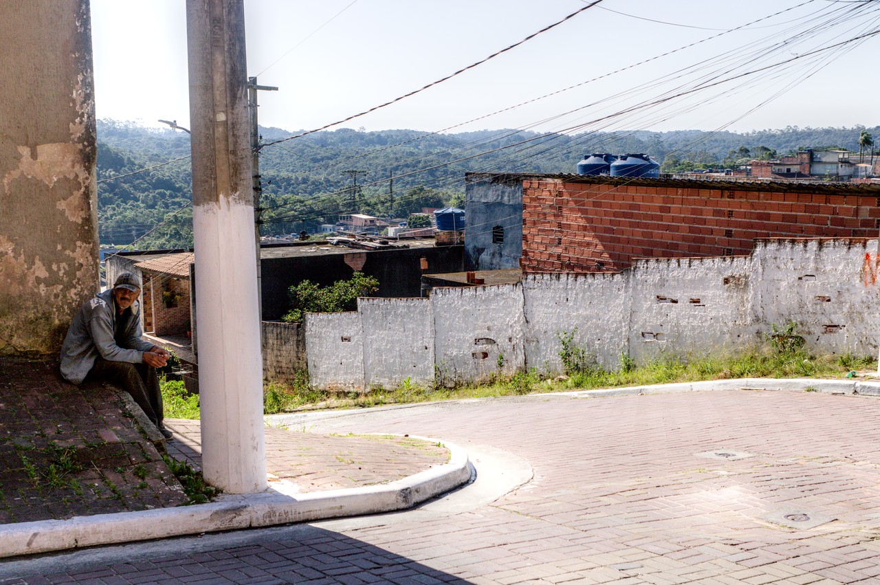 Rua periférica com serra florestada ao fundo.