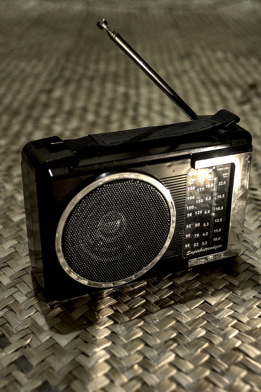 Rádio pequeno em cor preta à frente de fundo de palha.