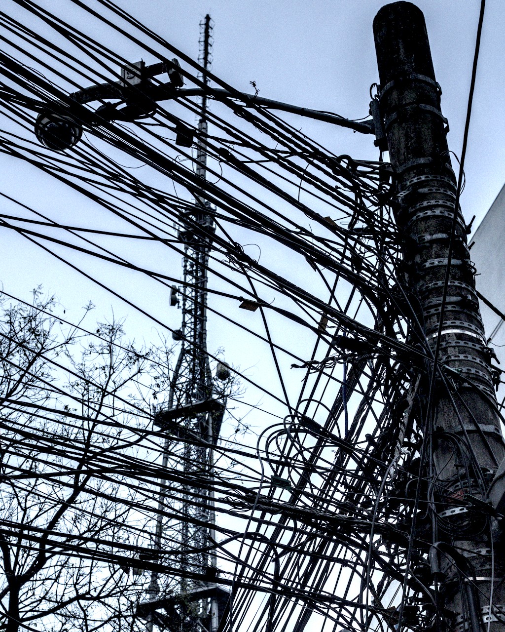 Torre da Globo atrás do caos de fios. Torre de telecomunicação ao funde escondida por fios de poste em primeiro plano.