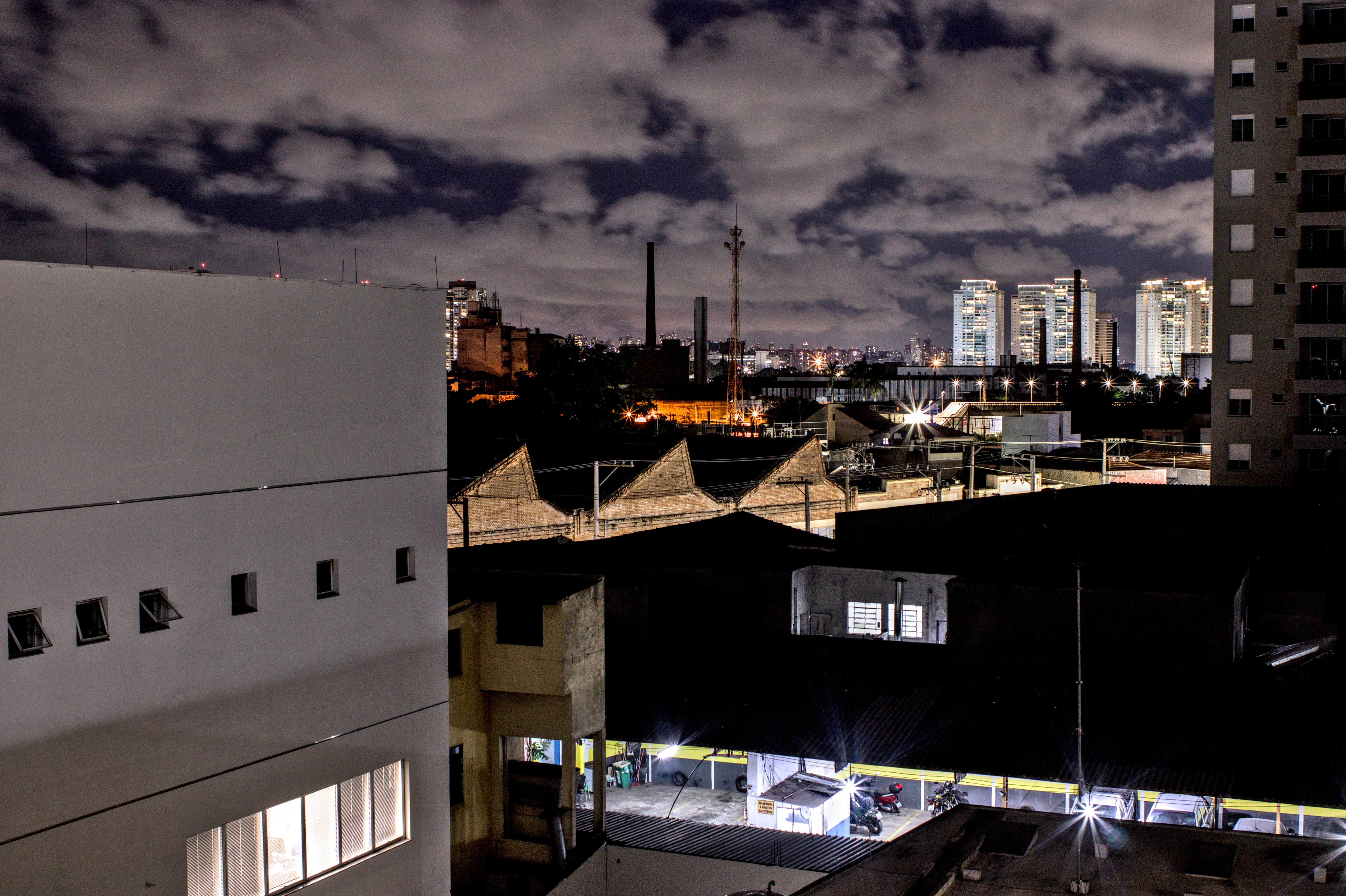 Visão noturna ampla. Luzes de postes em formato de estrela, construção de tijolos e prédios. O céu se ilumina com as luzes urbanas.