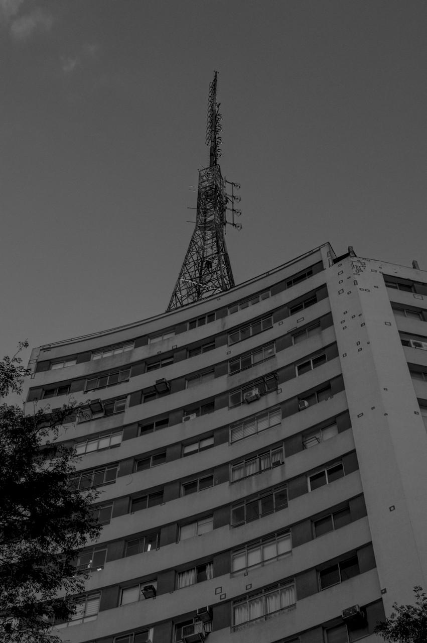 Contra-plongée de torre metálica sobre prédio modernista de alvernaria.