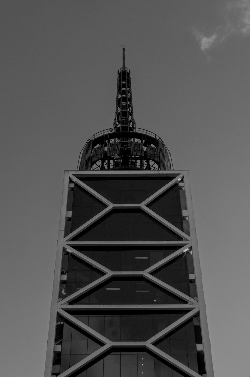 Contra-plongée de torre metálica sobre prédio envidraçado com estrutura mosaica.