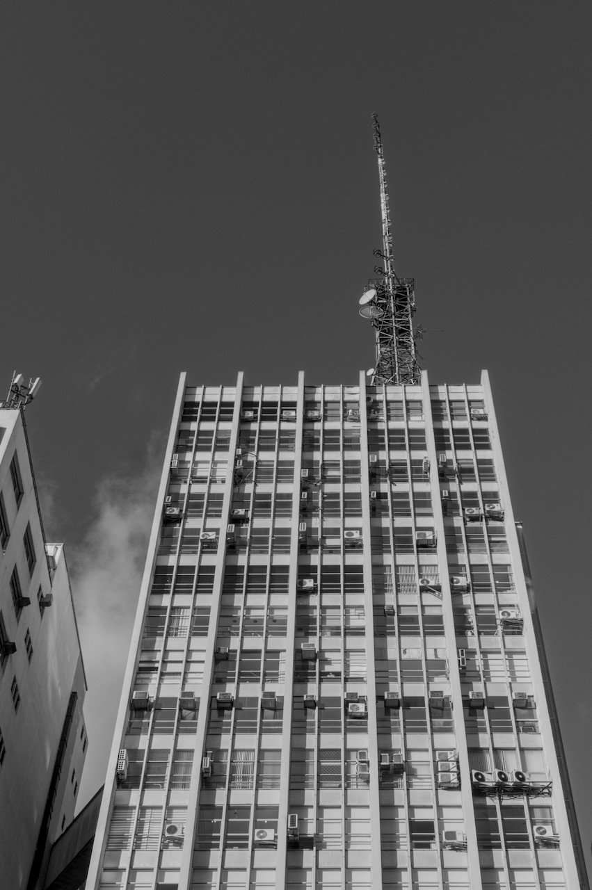 Contra-plongée de torre metálica alinhada à direita sobre prédio modernista.