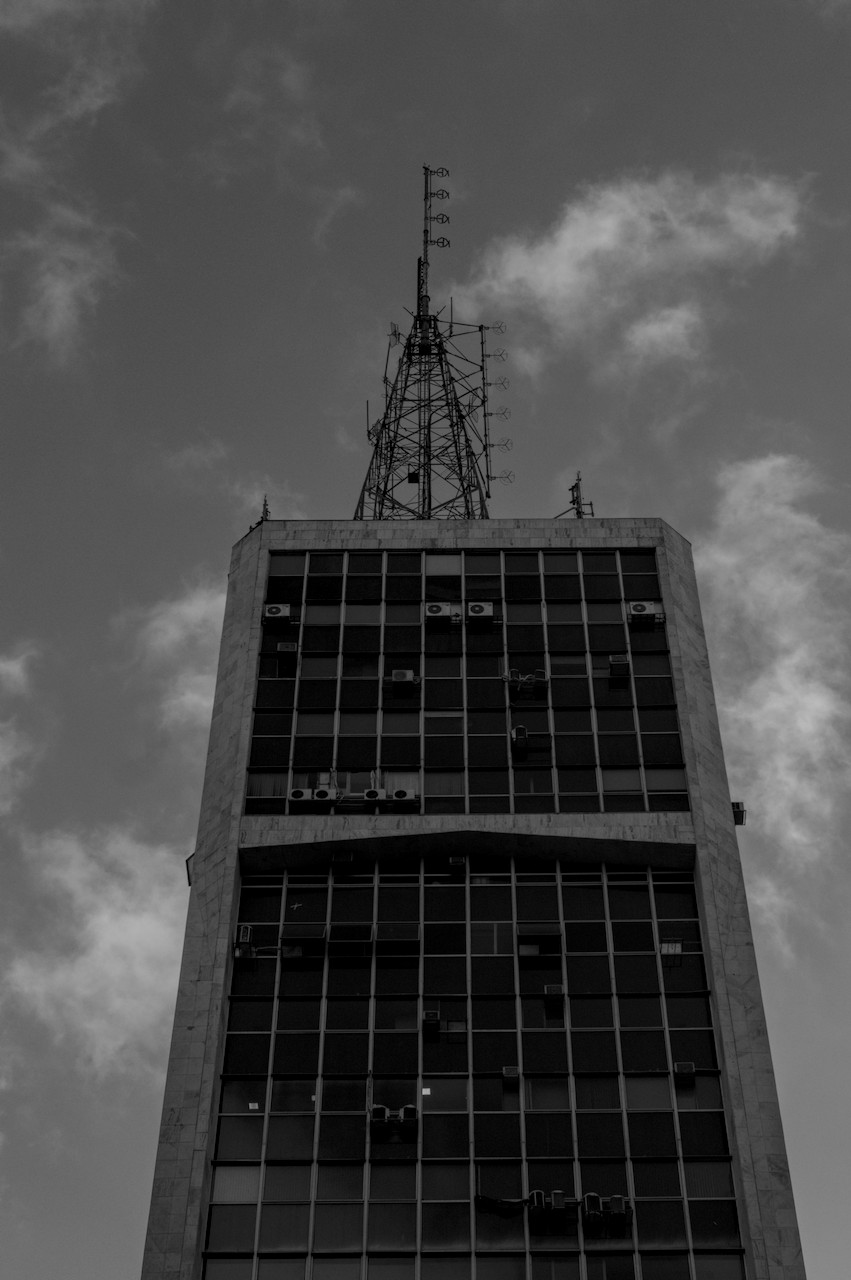 Contra-plongée de torre metálica sobre prédio envidraçado escuro.