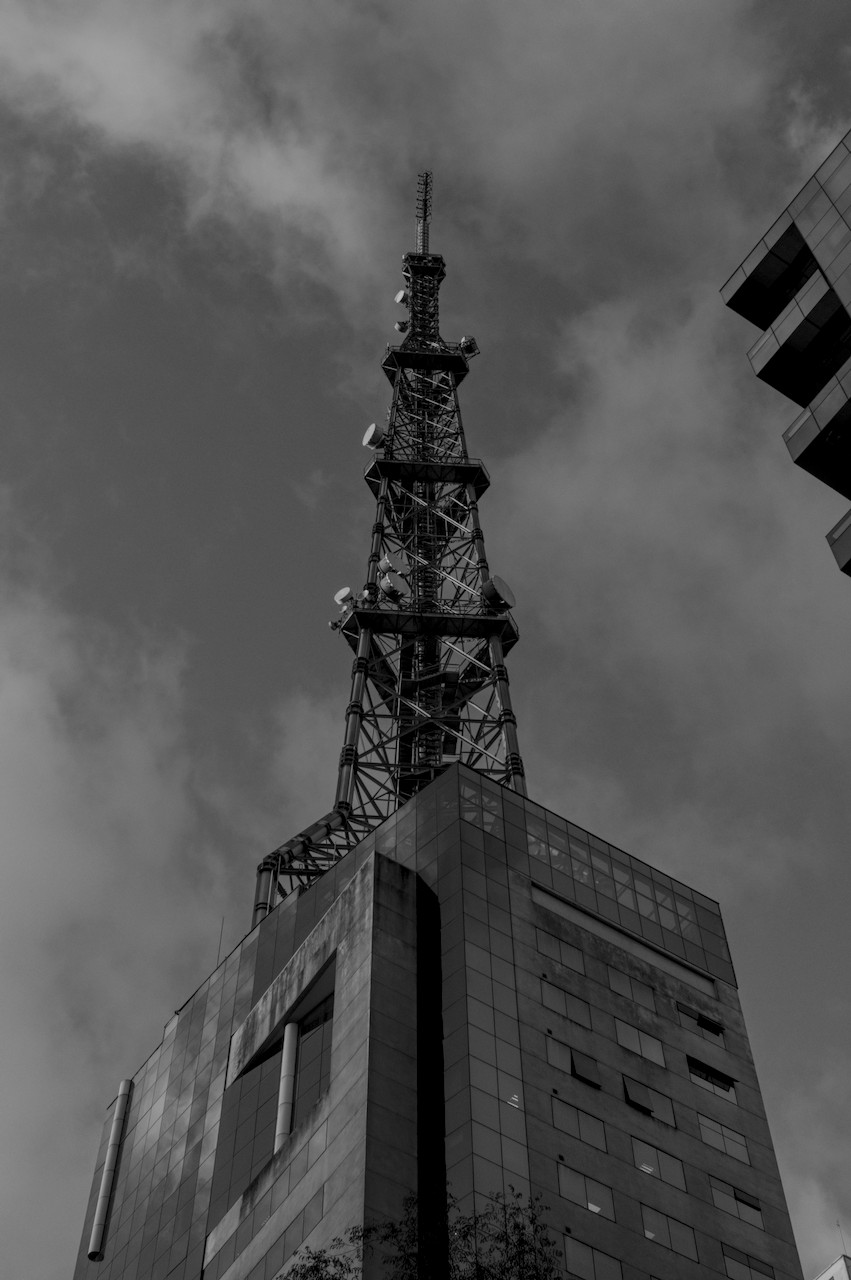 Contra-plongée oblícuo de torre metálica sobre prédio envidraçado.