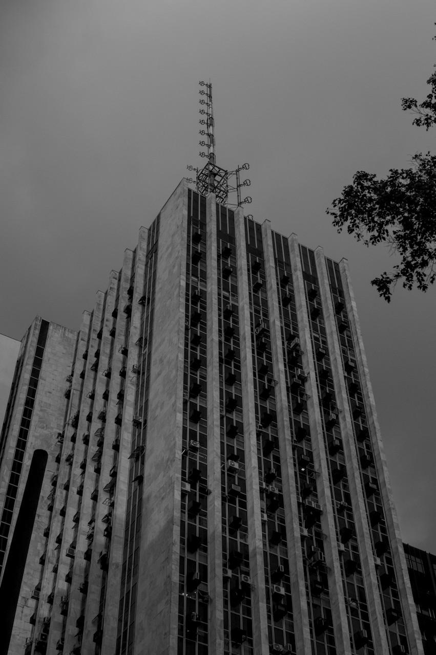 Contra-plongée oblícuo de torre metálica sobre prédio modernista.