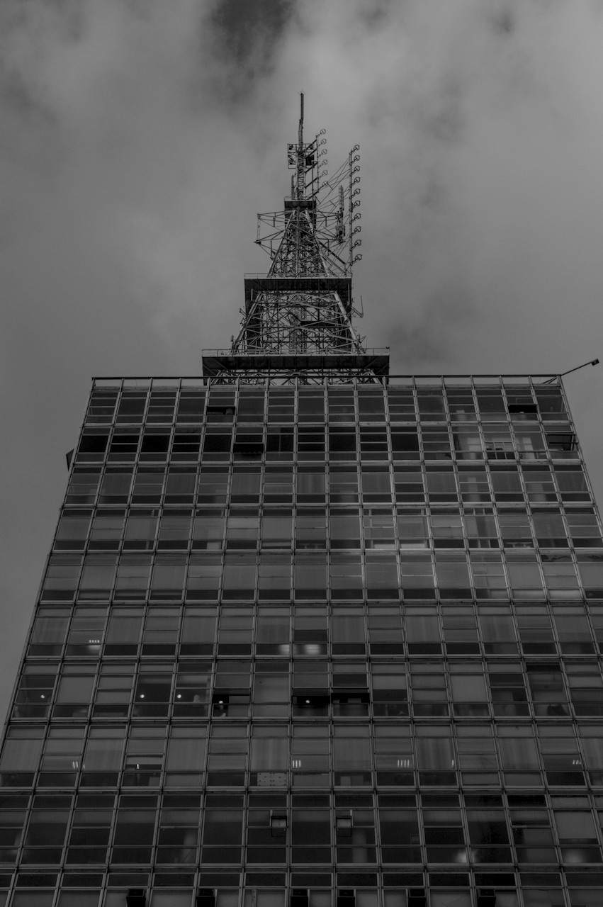 Contra-plongée de torre metálica sobre prédio envidraçado.