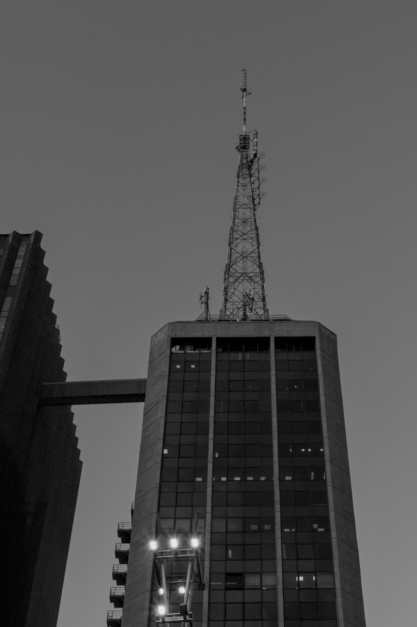 Contra-plongée de torre metálica sobre prédio envidraçado escuro.