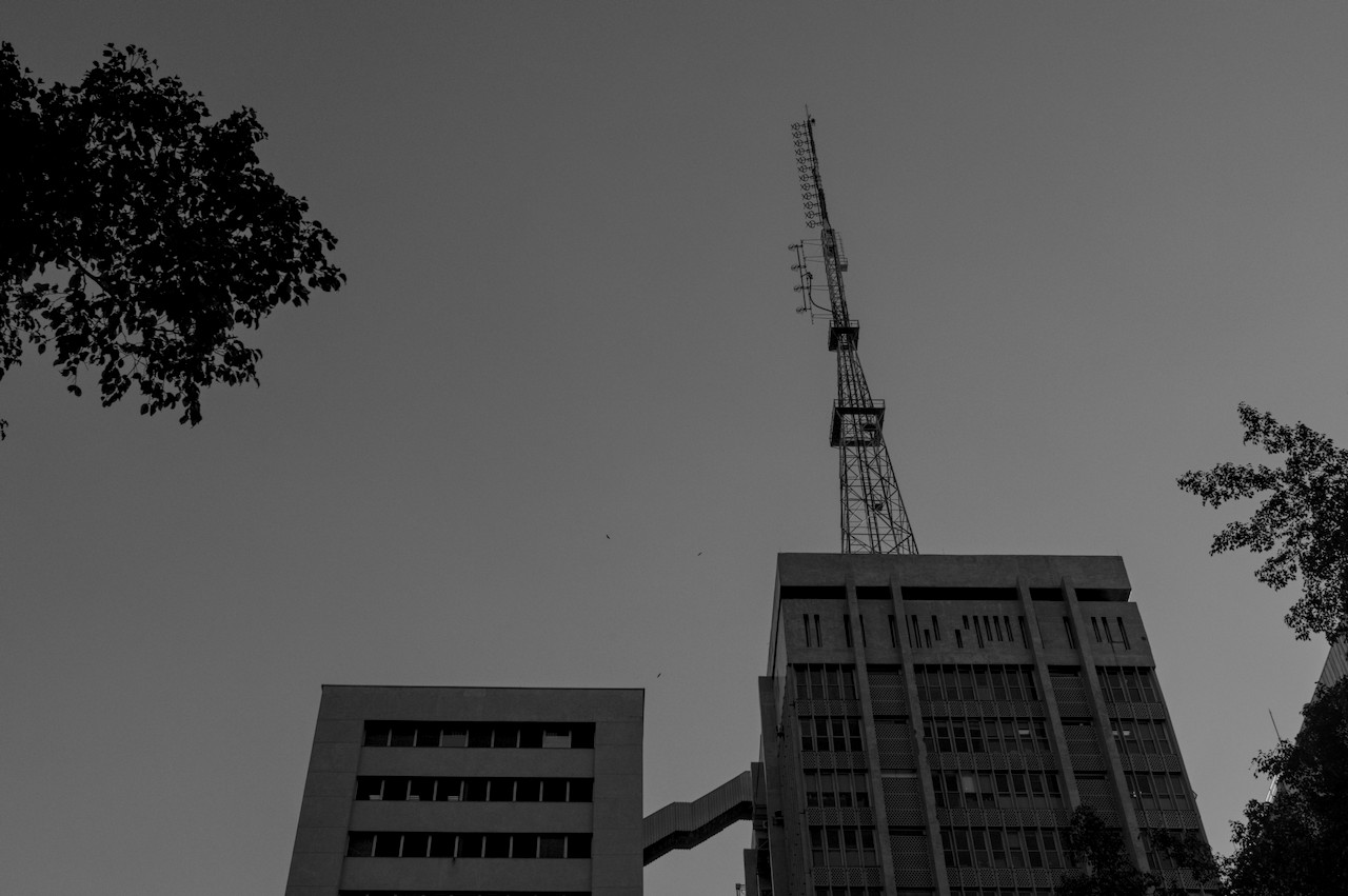Dois prédios conectados por passarela, sobre o da direita torre metálica.