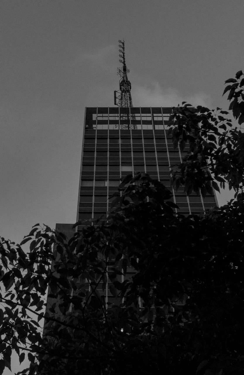 Contra-plongée de torre metálica sobre prédio envidraçado escuro.