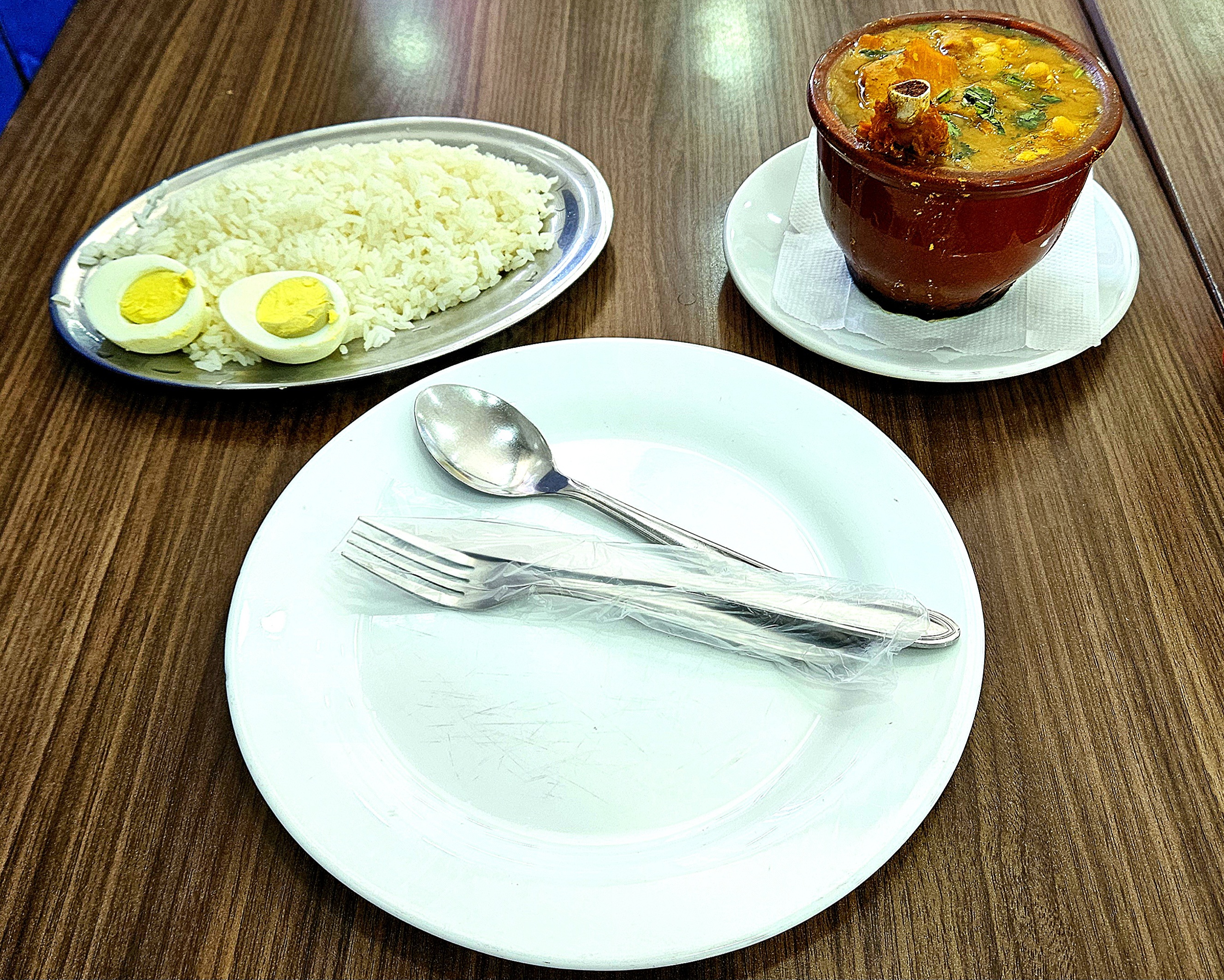 Prato com talheres, cuia de barro com dobradinha e prato de arroz com ovo cozido.