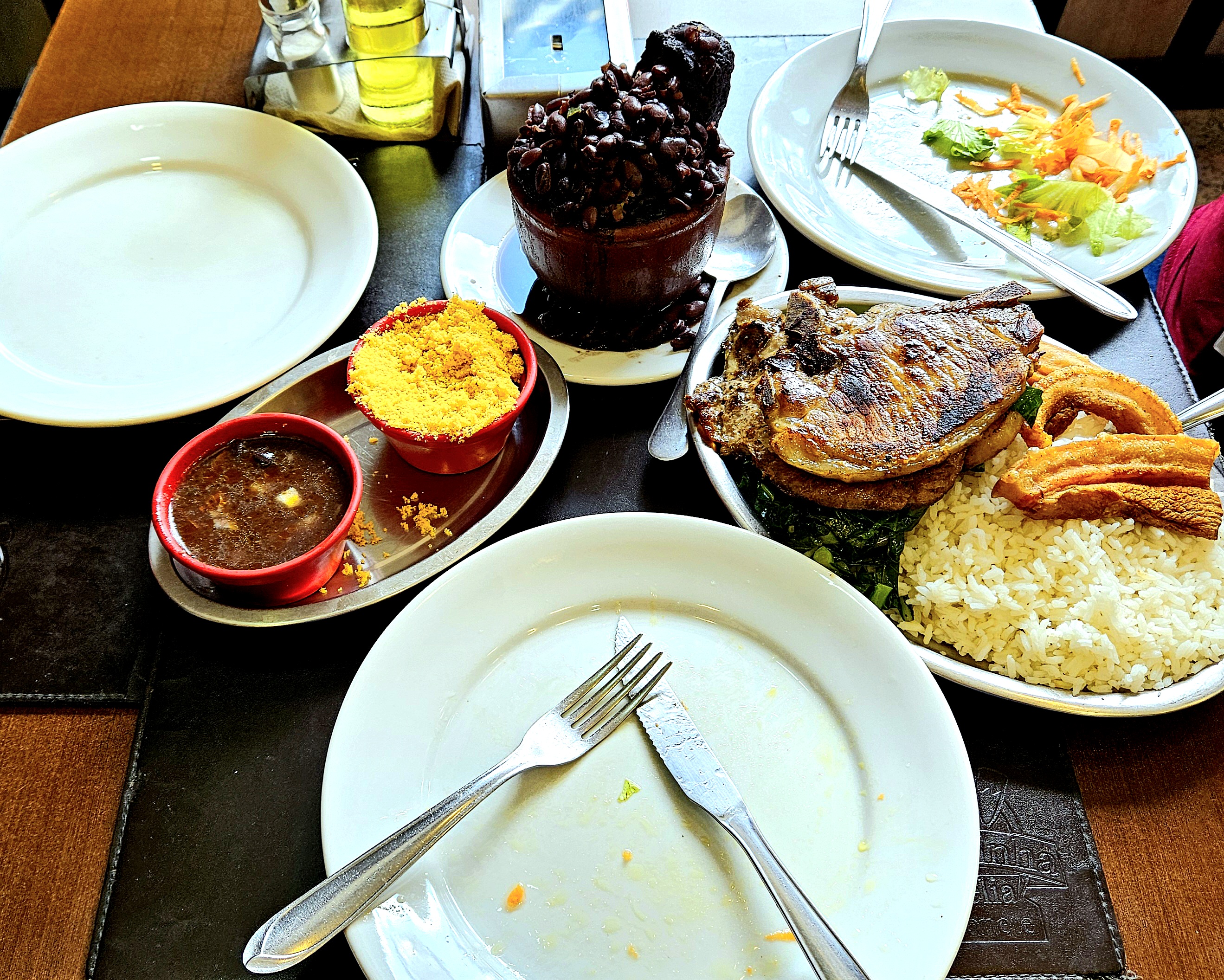 Mesa apertada com pratos, salada, cuia de barro com feijoada, prato de arrz com bisteca, couve e torresmo, potinhos de farofa e molho.