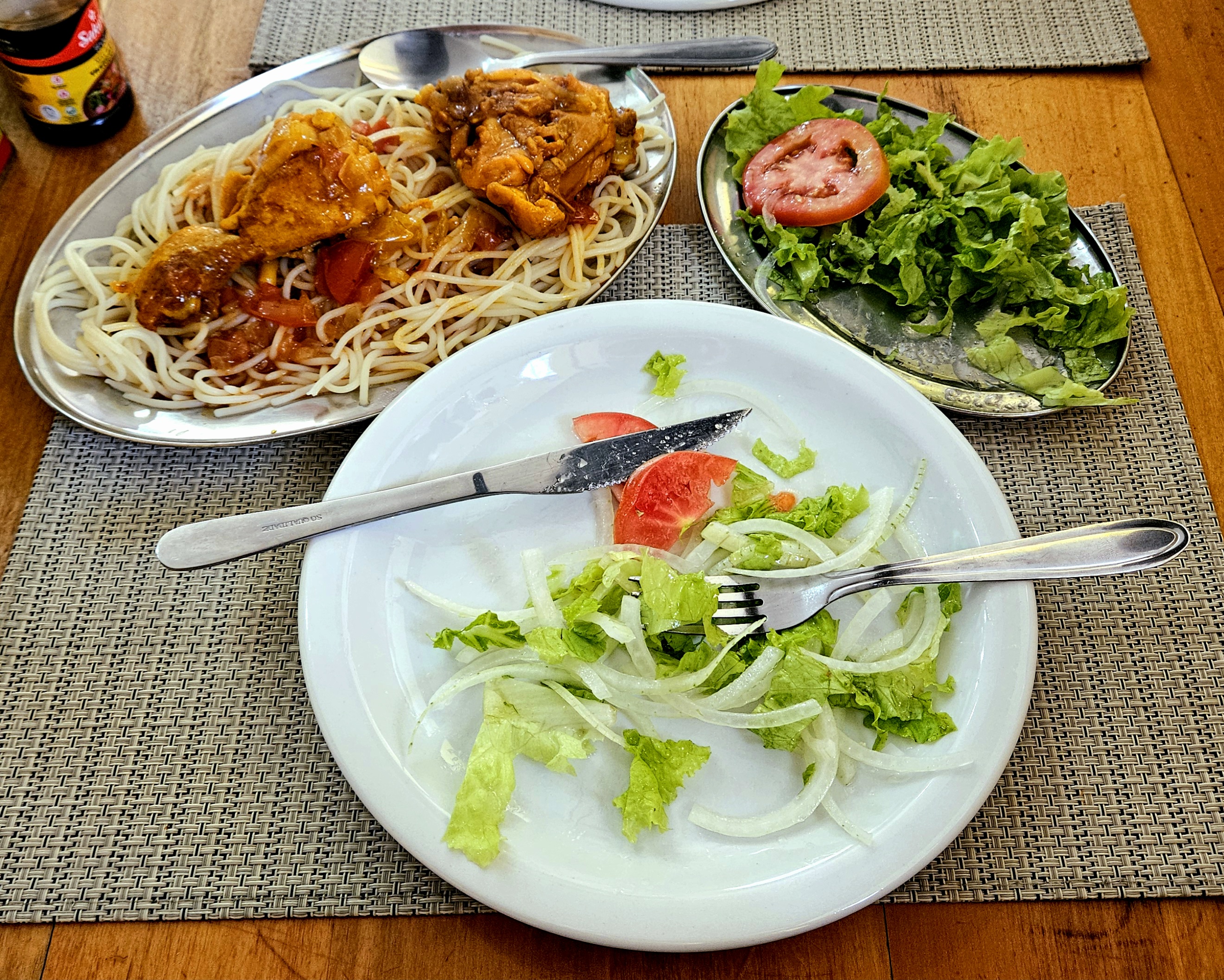 Prato com salada, prato de inox com salada e prato com macarrão e frango ao molho.