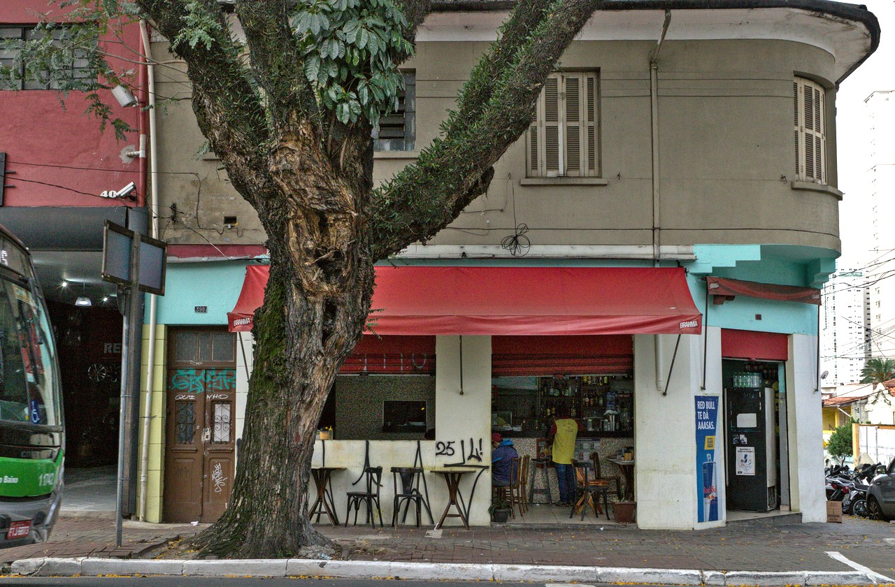 Boteco de esquina; homens consomem no balcão.